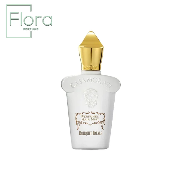 تصویر یک بطری عطر Xerjoff Casamorati Bouquet Ideale را نشان می‌دهد. این بطری سفید و شیک با طرحی بلند و دارای یک درپوش طلایی نوک‌دار است. روی بطری، نام “CASAMORATI” برجسته شده و در زیر آن، طراحی زیبا با نوشته‌های طلایی “PERFUMED HAIR MIST” و “BOUQUET IDEALE” قرار دارد.