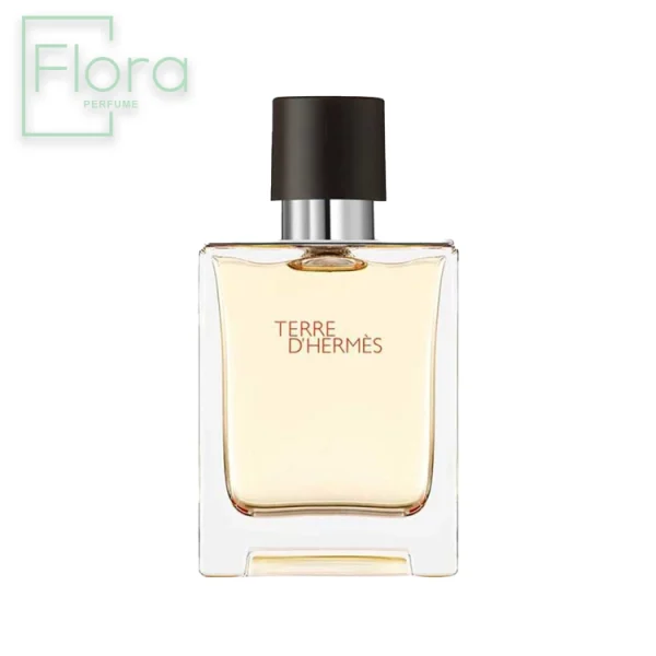 شیشه عطر مردانه تق د هرمس با طراحی ساده و شیک به تصویر کشیده شده است. شیشه شفاف با مایع درون آن کهربایی رنگ است و دربی به رنگ مشکی مات دارد. نام عطر “Terre d’Hermès” با فونتی ظریف روی شیشه حک شده است. لوگوی “Flora Perfume” نیز در گوشه بالا سمت چپ تصویر دیده می‌شود.