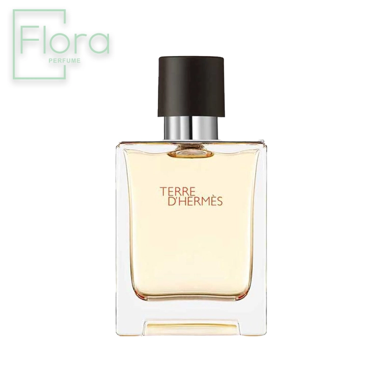 شیشه عطر مردانه تق د هرمس با طراحی ساده و شیک به تصویر کشیده شده است. شیشه شفاف با مایع درون آن کهربایی رنگ است و دربی به رنگ مشکی مات دارد. نام عطر “Terre d’Hermès” با فونتی ظریف روی شیشه حک شده است. لوگوی “Flora Perfume” نیز در گوشه بالا سمت چپ تصویر دیده می‌شود.