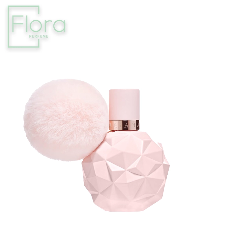 بطری عطر پرفیوم آریانا گرانده با طراحی منحصر به فرد و رنگ صورتی، دارای یک پوم پوم خزدار کوچک به رنگ مشابه در کنار درب بطری است. لوگوی برجسته “Flora Perfume” در بالای تصویر دیده می‌شود.