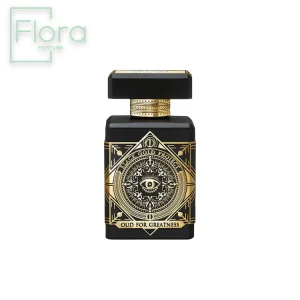 تصویر نمای نزدیک از بطری عطر Initio Oud for Greatness. بطری مشکی رنگ با طراحی هندسی و تزئینات طلایی است. در قسمت جلویی بطری، یک دایره طلایی با طرح چشم قرار دارد و در پایین آن عبارت “OUD FOR GREATNESS” نوشته شده است. درپوش بطری مشکی رنگ و مکعبی شکل است.